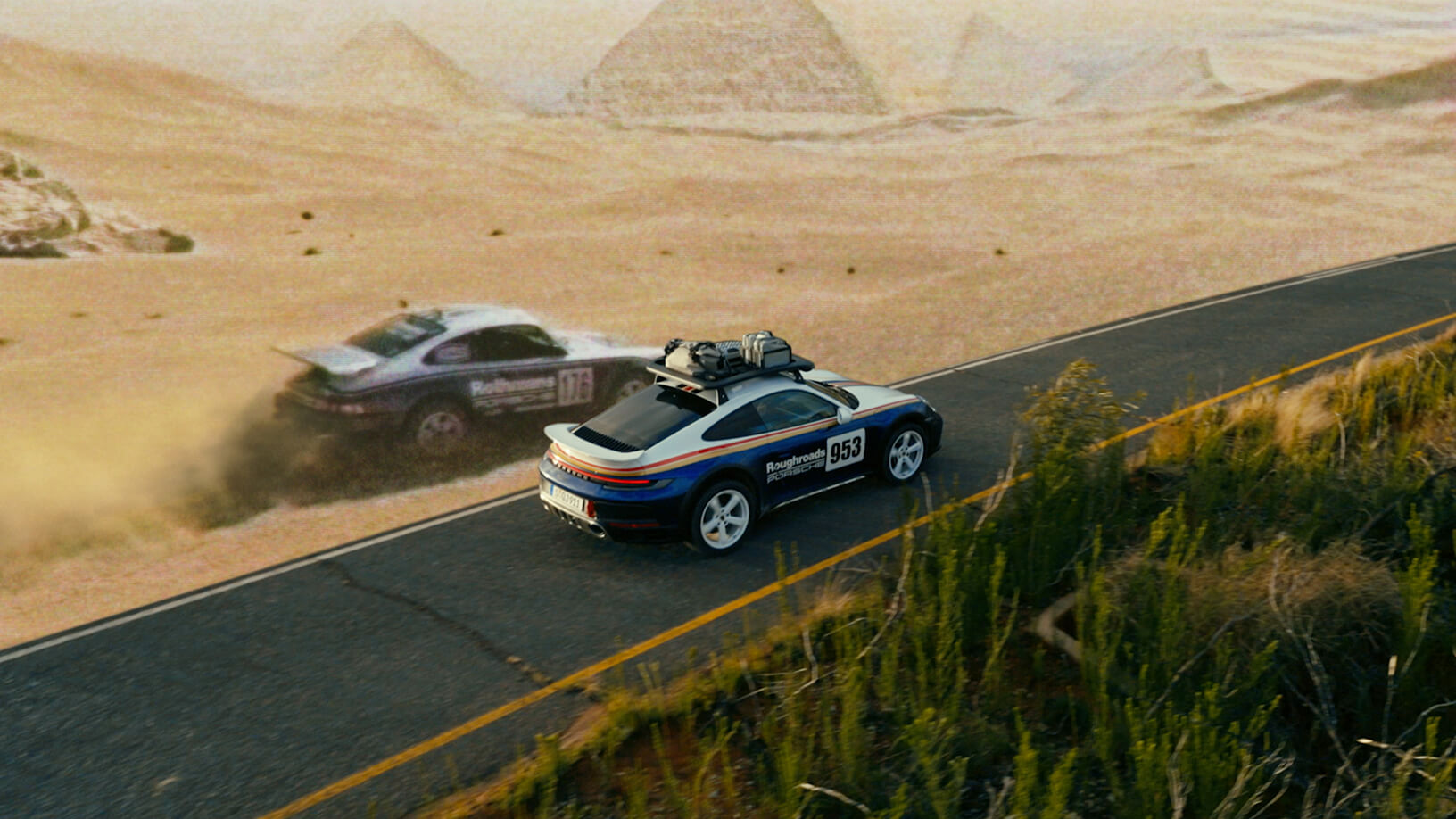 Two Porsche rally cars seen from above on a winding desert road.